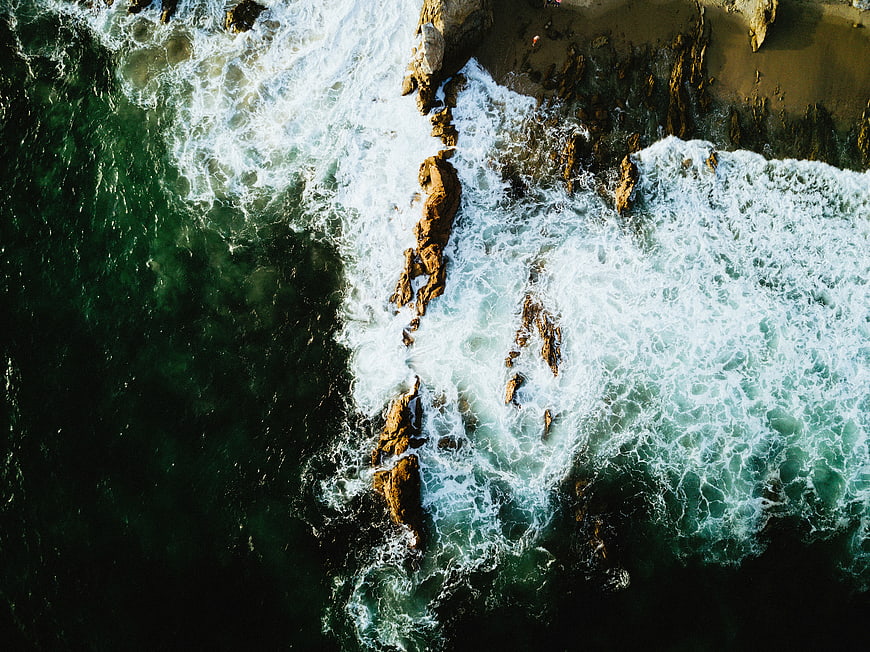 Aerial view of ocean waves crashing against rocky coastline