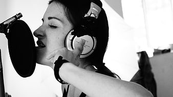 Woman singing into microphone with headphones in recording studio