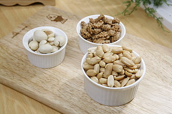 Three white bowls of peanuts, ginkgo nuts, and sesame balls on wood