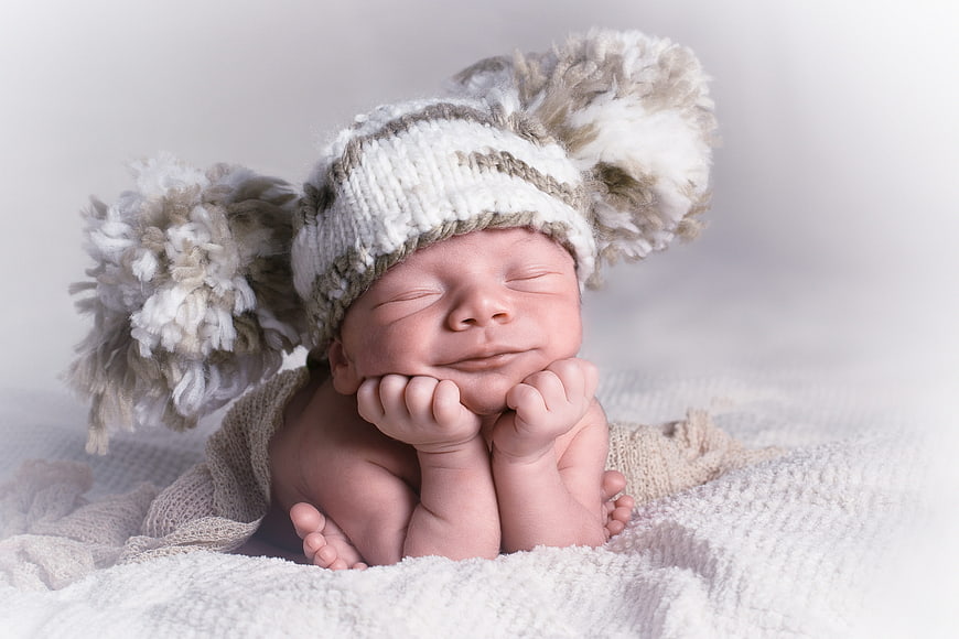 Sleeping newborn baby wearing a knitted bear ear hat on a white blanket