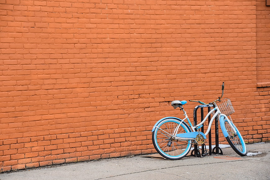 Blue and white bicycle parked against orange brick wall