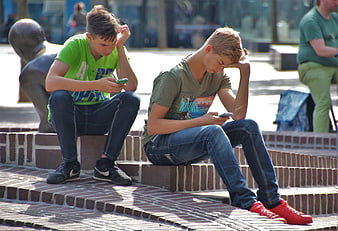 Two Teenage Boys Playing Mobile Games on Brick Steps