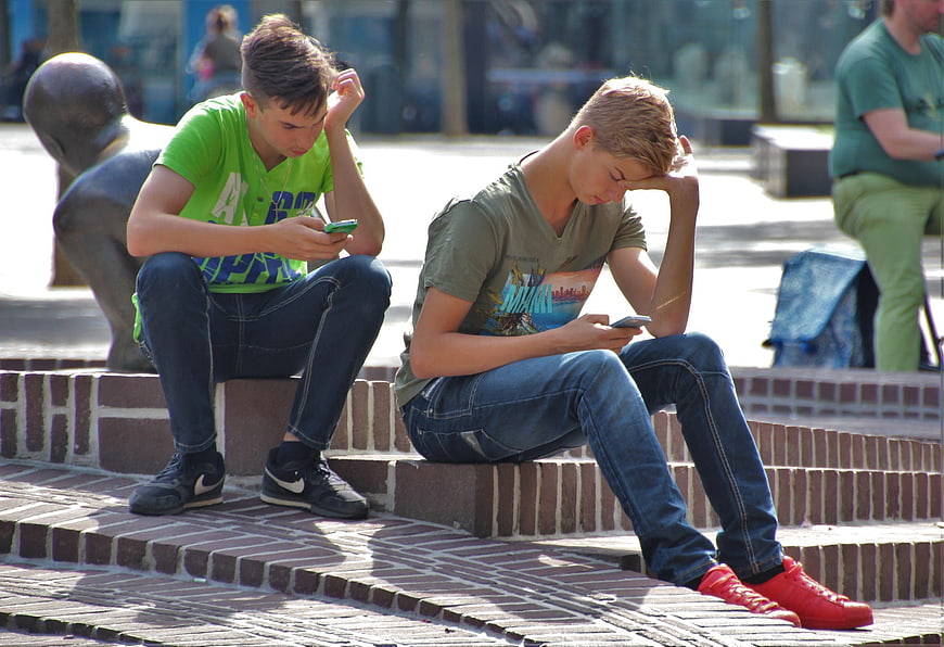 Two Teenage Boys Playing Mobile Games on Brick Steps
