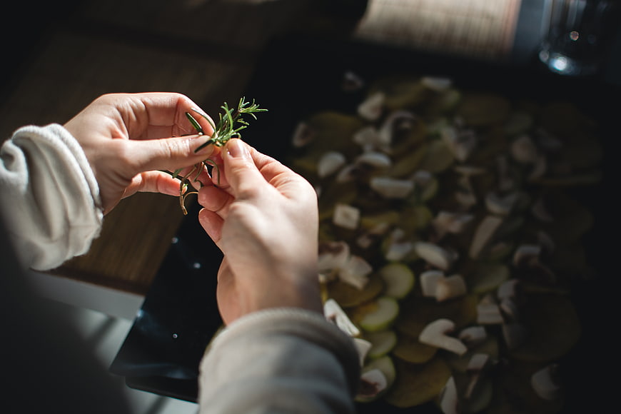 Hands Stripping Rosemary Sprig Over Chopped Vegetables