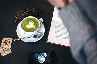 Overhead view of matcha latte with heart art, book, and smartphone