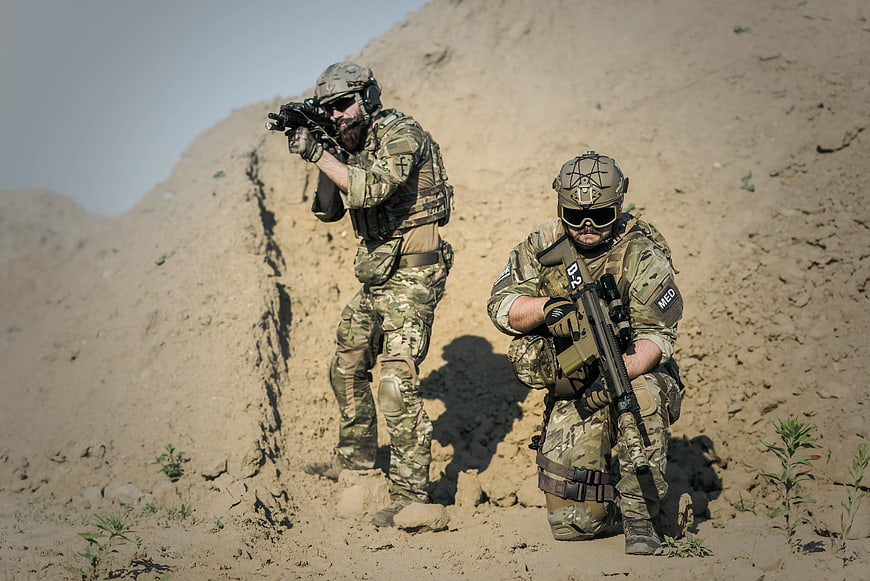 Two soldiers in tactical gear aiming rifles in desert terrain