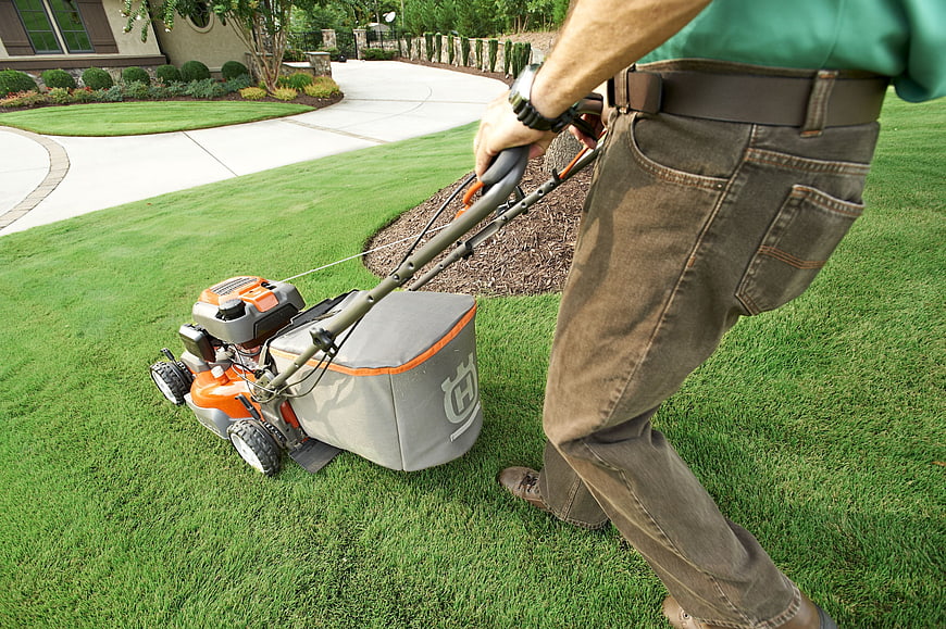 Man mowing a green lawn with a push mower in a suburban garden