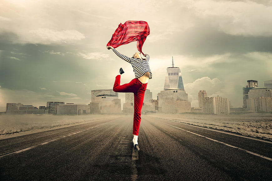 Woman dancing on road with red scarf against city skyline