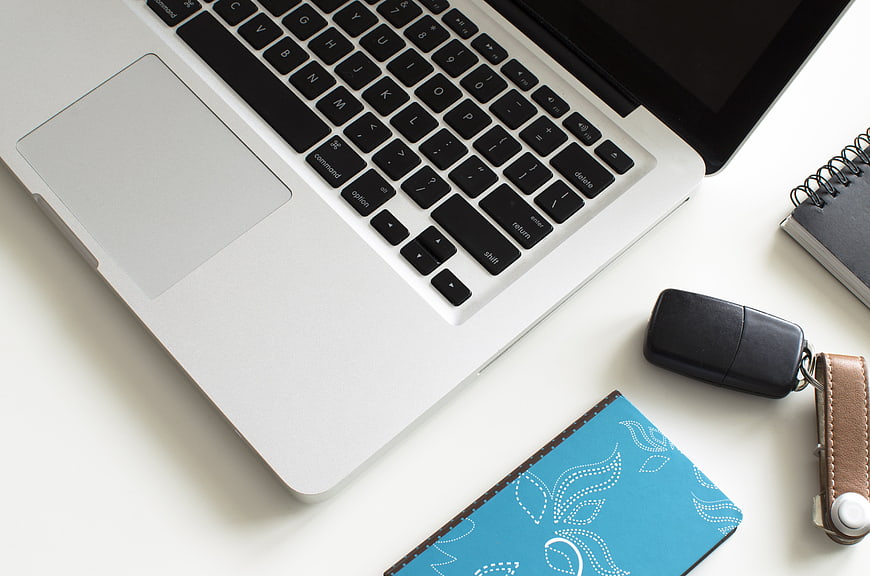 Top-Down View of MacBook, Blue Wallet, and Car Key on White Desk