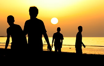 Silhouette of friends walking on beach at sunset
