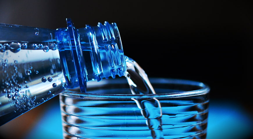 Close-up of Sparkling Water Pouring from Blue Bottle into Glass