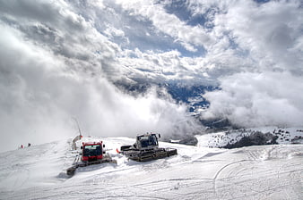 Snow groomers on a mountain peak above the clouds