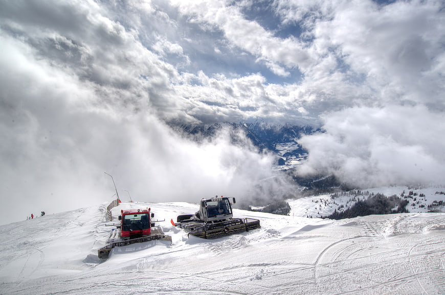 Snow groomers on a mountain peak above the clouds