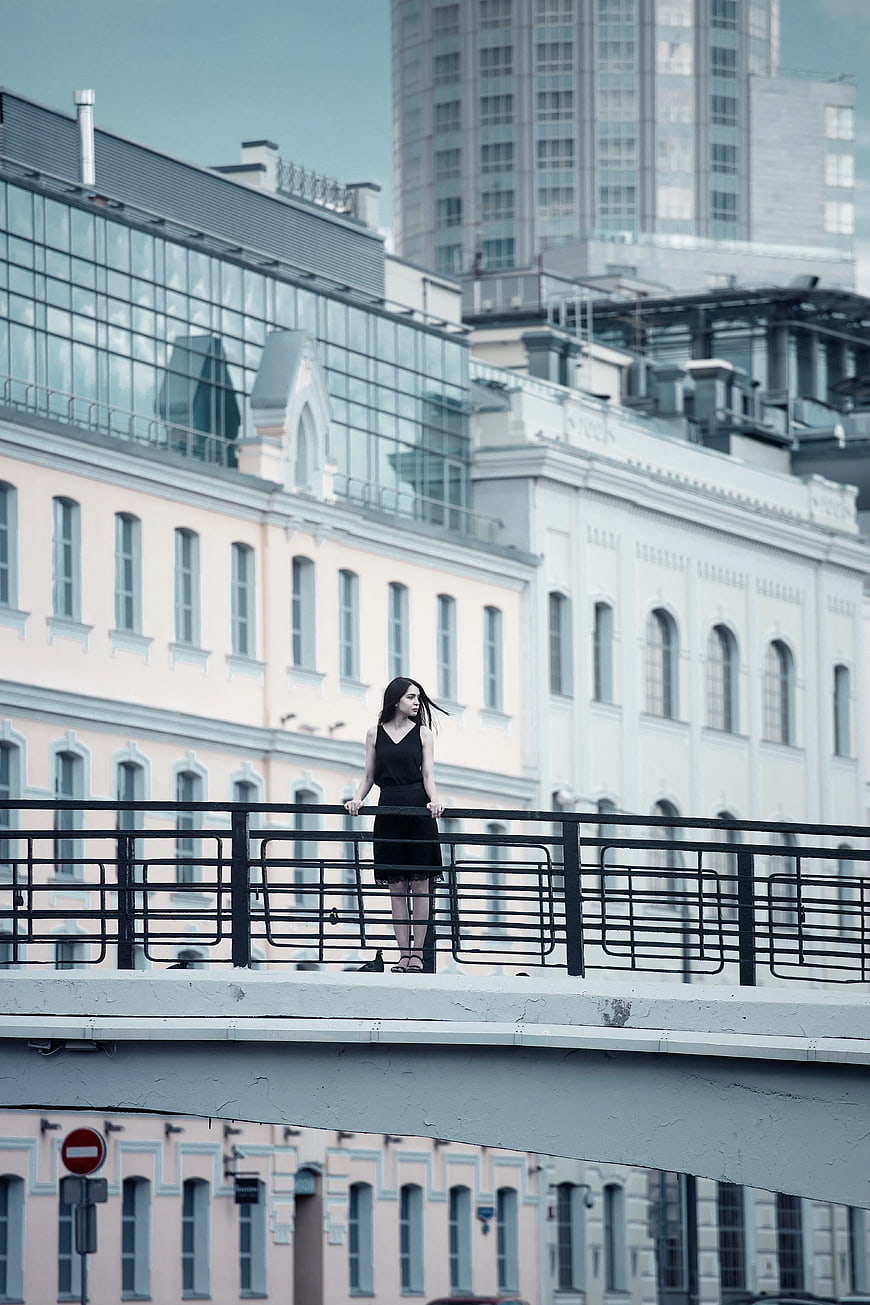 Woman in black dress standing on urban bridge railing