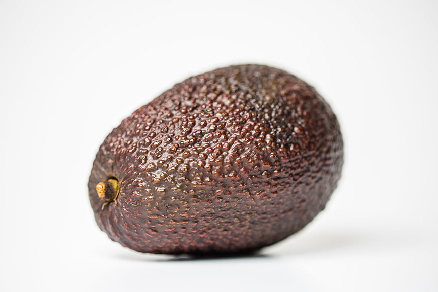Single ripe Hass avocado with textured skin on white background