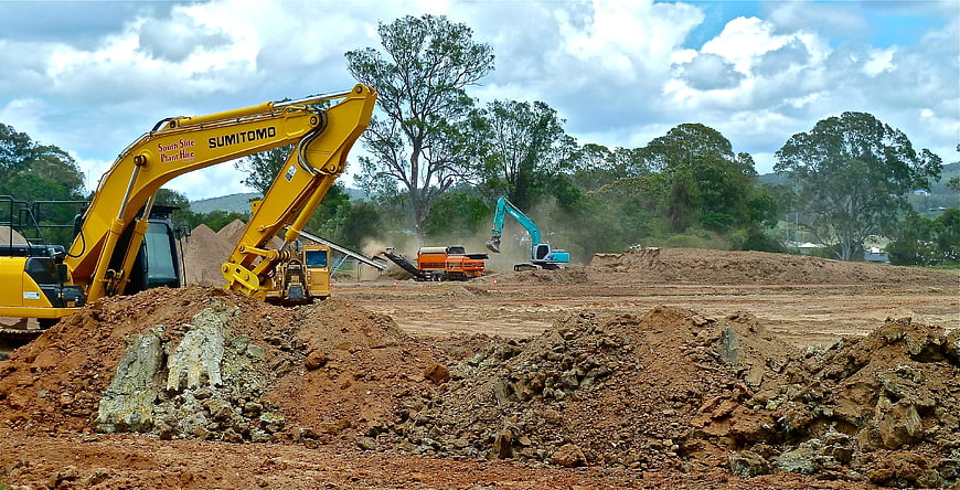 Heavy Excavators Working on Construction Site with Dirt Piles
