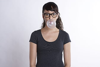 Young woman with glasses blowing a bubblegum bubble against a white background