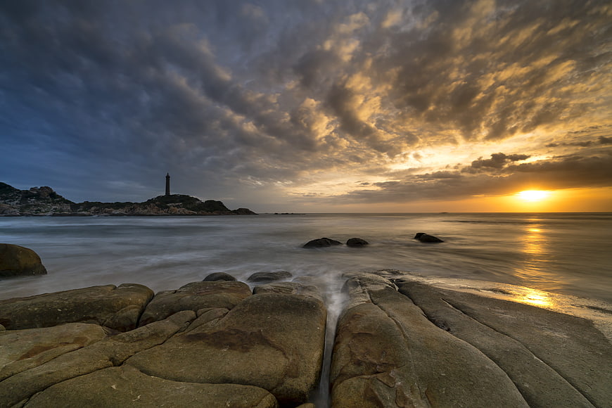 Dramatic Sunset Over Rocky Coastline with Lighthouse