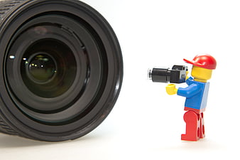 Lego minifigure photographer with camera facing large camera lens on white background
