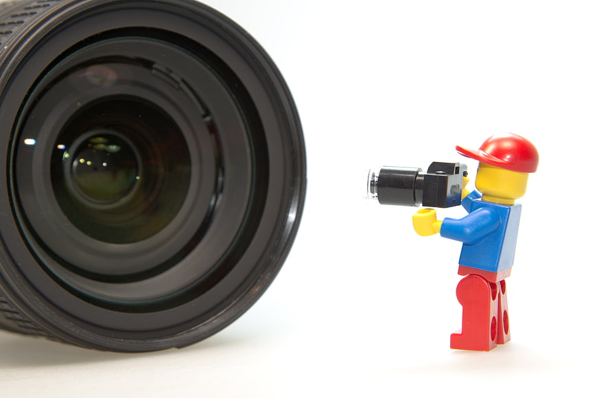 Lego minifigure photographer with camera facing large camera lens on white background