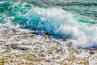 Crashing turquoise ocean wave with white foam on sandy beach