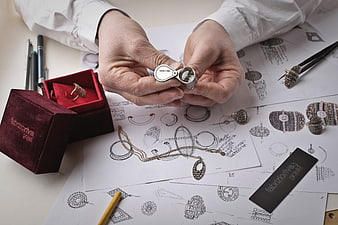 Jewelry designer hands examining silver ring over sketches