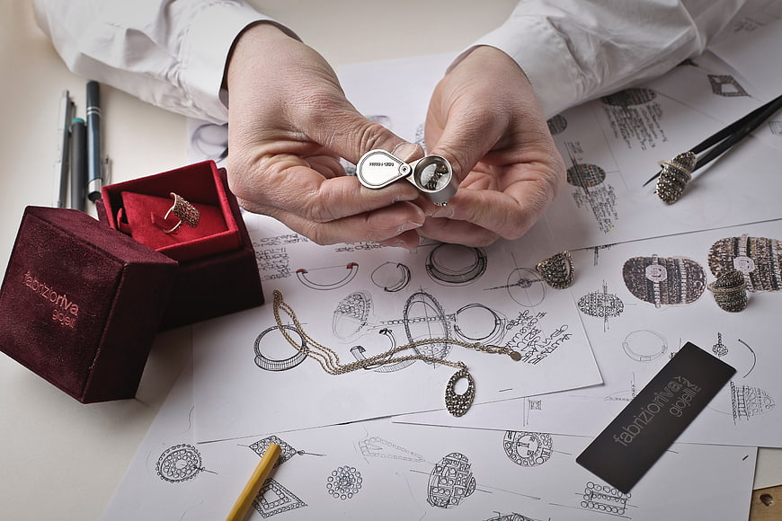 Jewelry designer hands examining silver ring over sketches