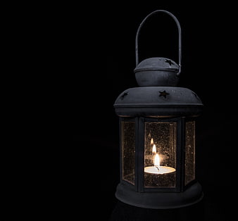 Vintage black lantern with lit candle on black background