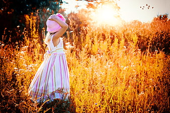 Little Girl in Pink Hat Standing in Golden Field at Sunset