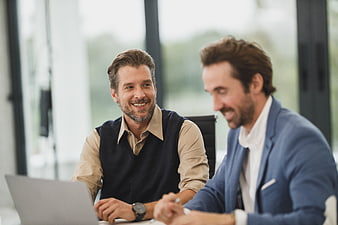 Two smiling businessmen collaborating at a laptop in a modern office