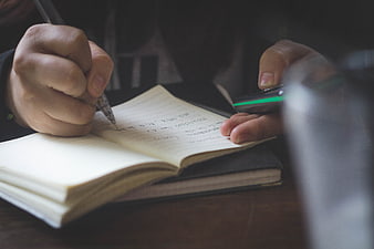 Close-up of hands writing in notebook while holding smartphone