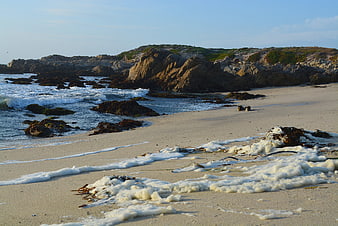 Sandy beach with ocean waves and rocky cliffs at sunset