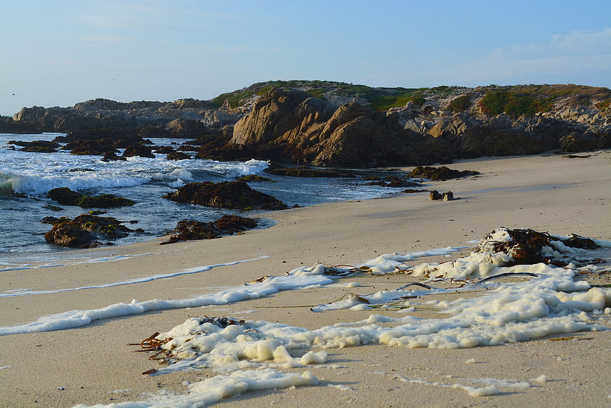 Sandy beach with ocean waves and rocky cliffs at sunset