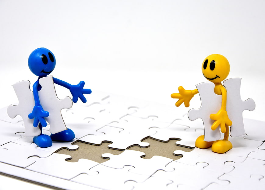 Blue and yellow figurines holding puzzle pieces on white background