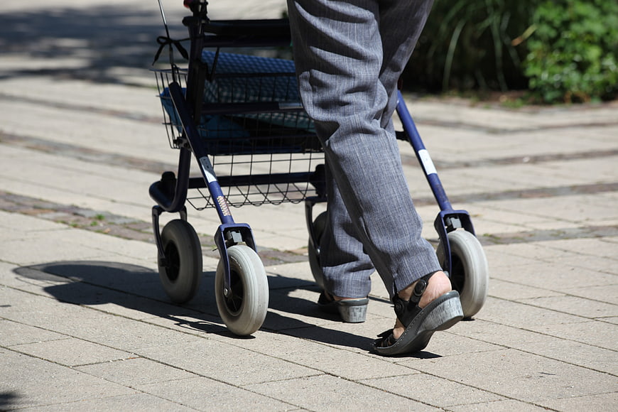 Senior Woman Walking With Blue Rollator On Paved Path