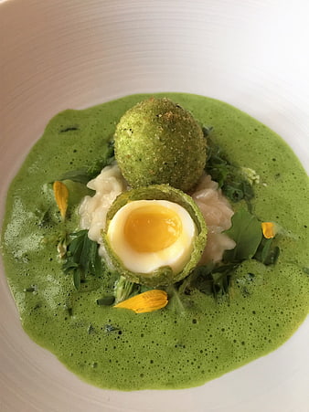 Gourmet green soup with scotch egg and yellow flower garnish