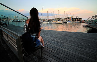 Woman Sitting on Dock Bench Watching Sunset Over Marina