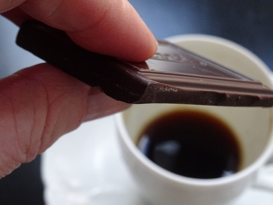 Hand holding dark chocolate bar over espresso cup