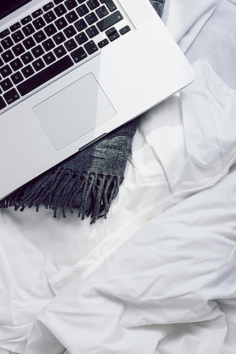 Silver laptop on white bed sheets with gray scarf