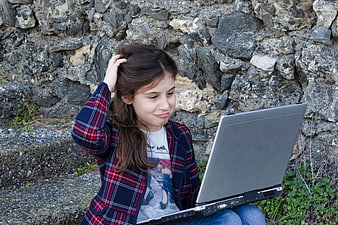 Young girl using laptop outdoors against stone wall