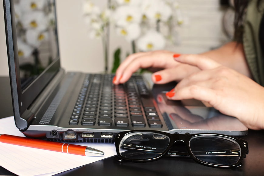 Woman Typing on Laptop with Glasses and Pen