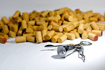 Silver corkscrew with pile of wine corks on white background