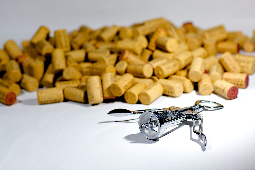 Silver corkscrew with pile of wine corks on white background