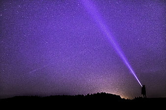Silhouette of Person Shining Flashlight into Starry Night Sky