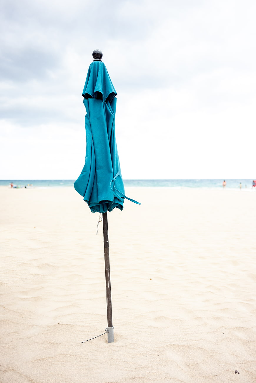 Closed Teal Beach Umbrella on Sandy Shore with Ocean Background