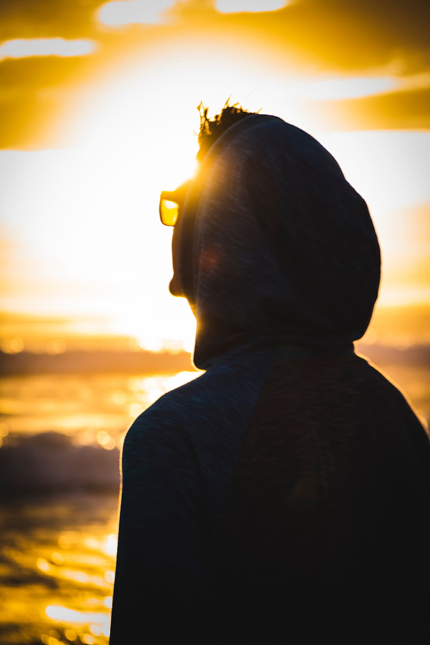 Silhouette of Man in Hoodie Watching Golden Sunset Over Ocean