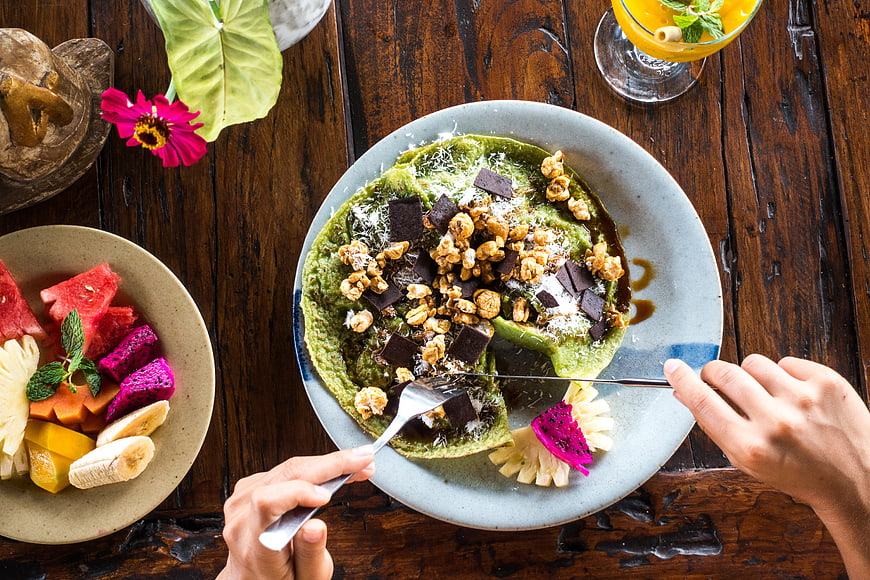 Top View of Matcha Pancakes with Tropical Fruit and Hands Eating