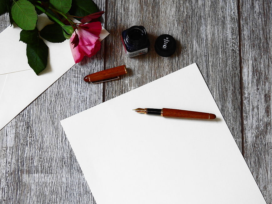 Fountain pen, ink, and rose on rustic wooden background