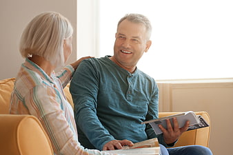 Happy senior couple reading and smiling on sofa at home