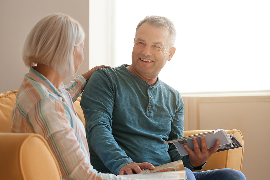 Happy senior couple reading and smiling on sofa at home
